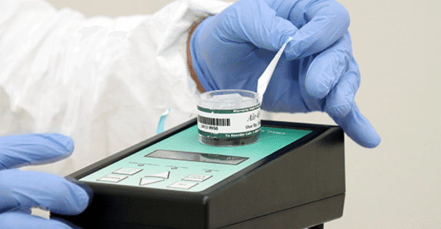 Gloved hand placing a labeled air sample cassette onto a sampling pump