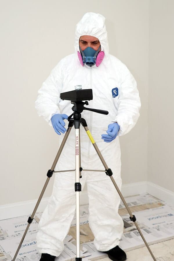 Inspector in full PPE with an air sampling pump mounted on a tripod