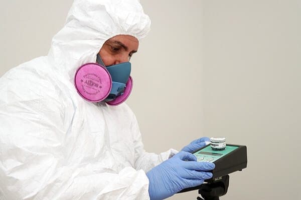 Inspector in PPE and a respirator holding a sample collection jar